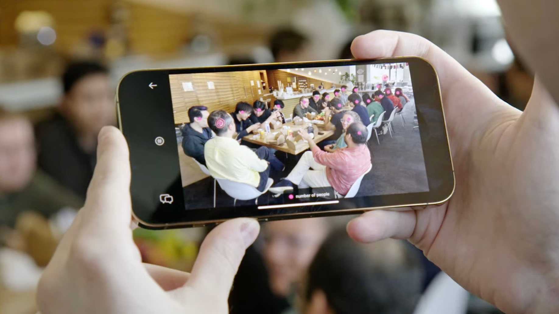 An image of a man holding a phone taking a pictuer of a group of people at a table.